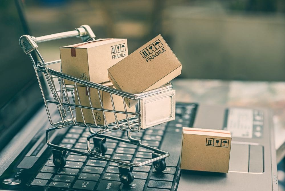 A small shopping cart filled with boxes, symbolizing online shopping, rests on a laptop keyboard, representing the convenience of e-commerce and digital transactions.