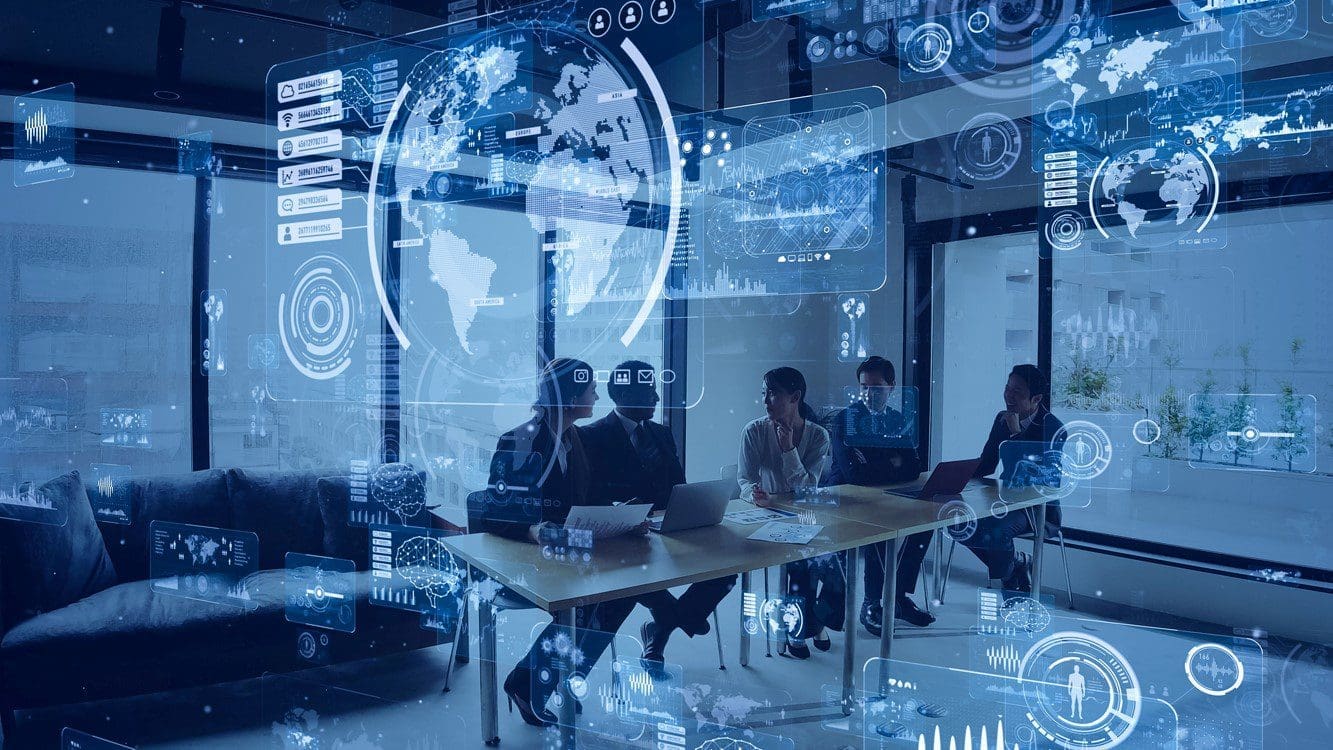 onnected world. In the background, five individuals are seated around a table with laptops, engaged in a collaborative meeting, representing teamwork and connectivity in a technology-driven environment.